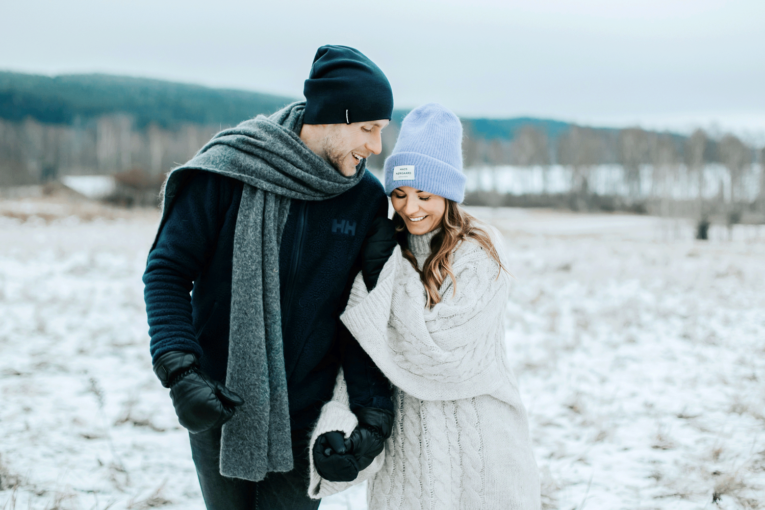 Malin och Per Åslund som håller om varandra i sin parfotografering. Vinter så båda har mössa och halsduk på sig.