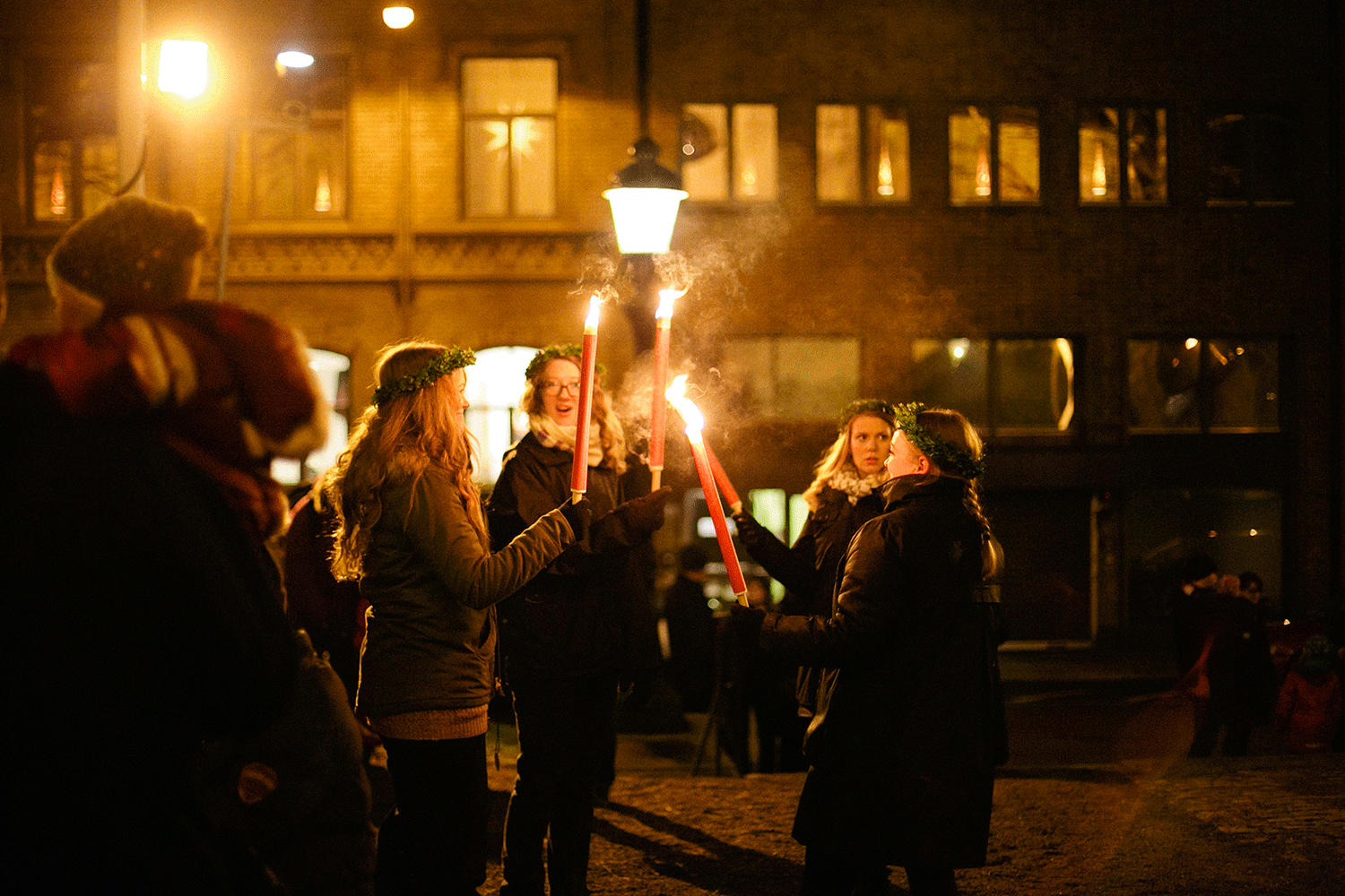 Luciatåget i Karlstad domkyrka tänder facklor för att gå fackeltåg. Fyra kvinnor som står med facklor framför ljuslykta.