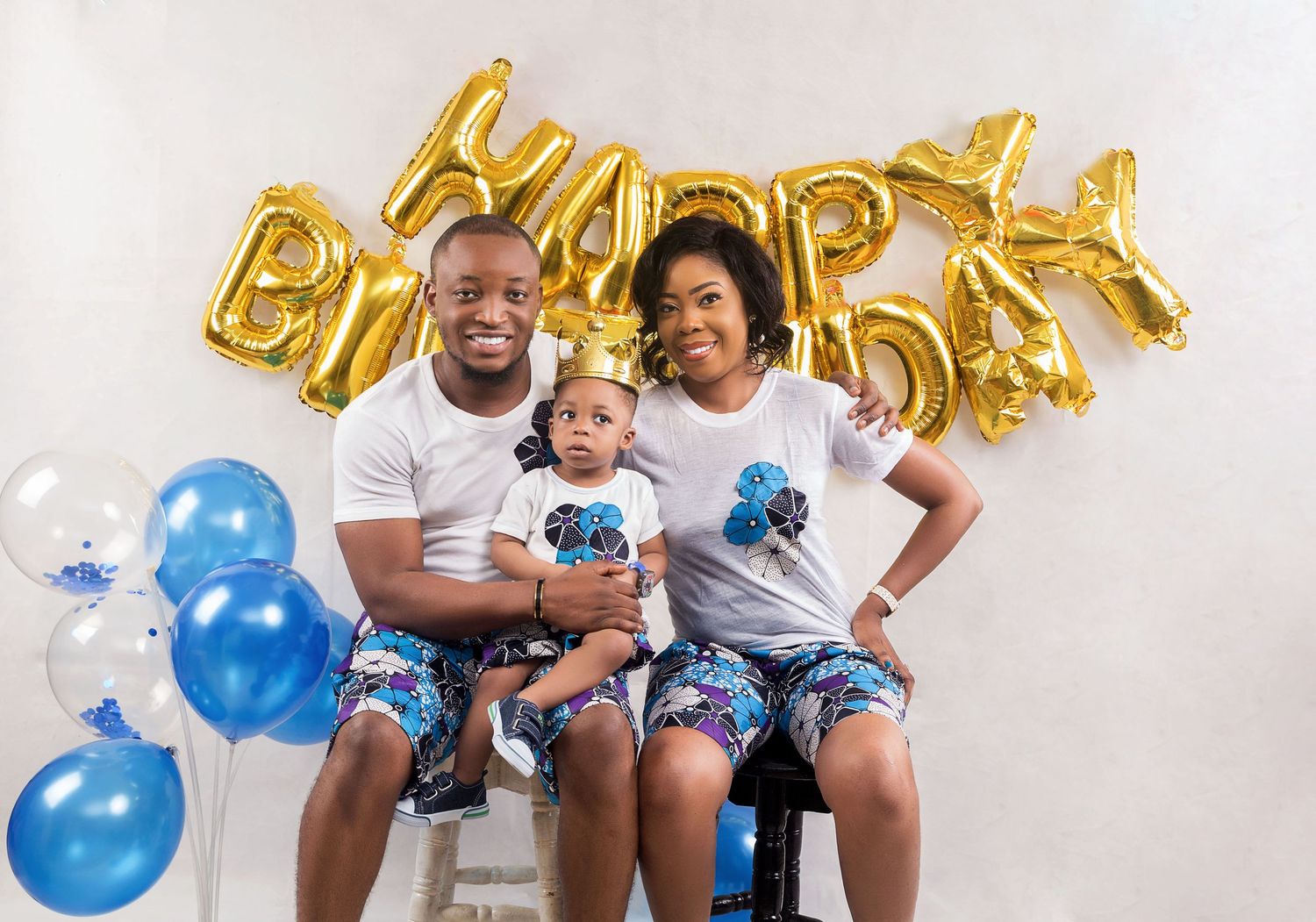 Happy family of three in matching outfits celebrating a birthday with blue and white balloons.