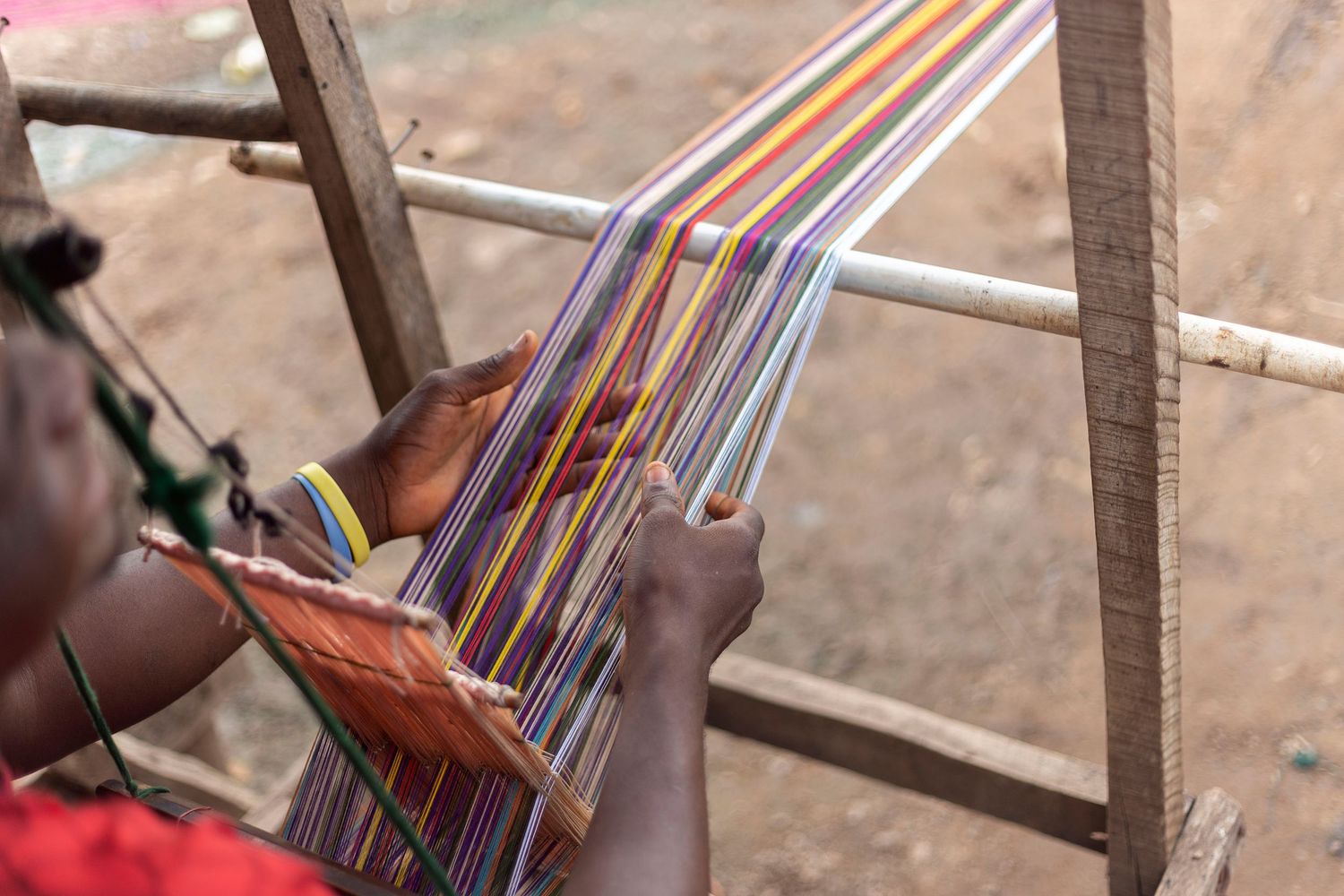 Close-up of hands weaving colorful striped fabric on a traditional wooden loom in Africa.