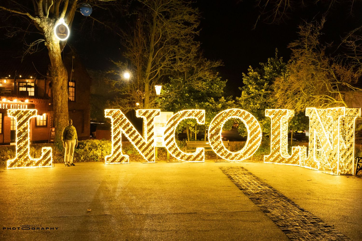 Illuminated LINCOLN sign with golden light-up letters displayed outdoors at night in a festive holiday setting.