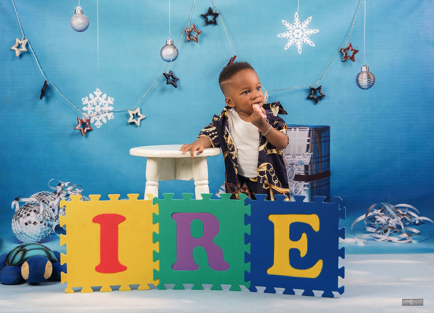 Smiling baby boy sitting with colorful foam letters IRE in a festive blue winter holiday photo shoot.