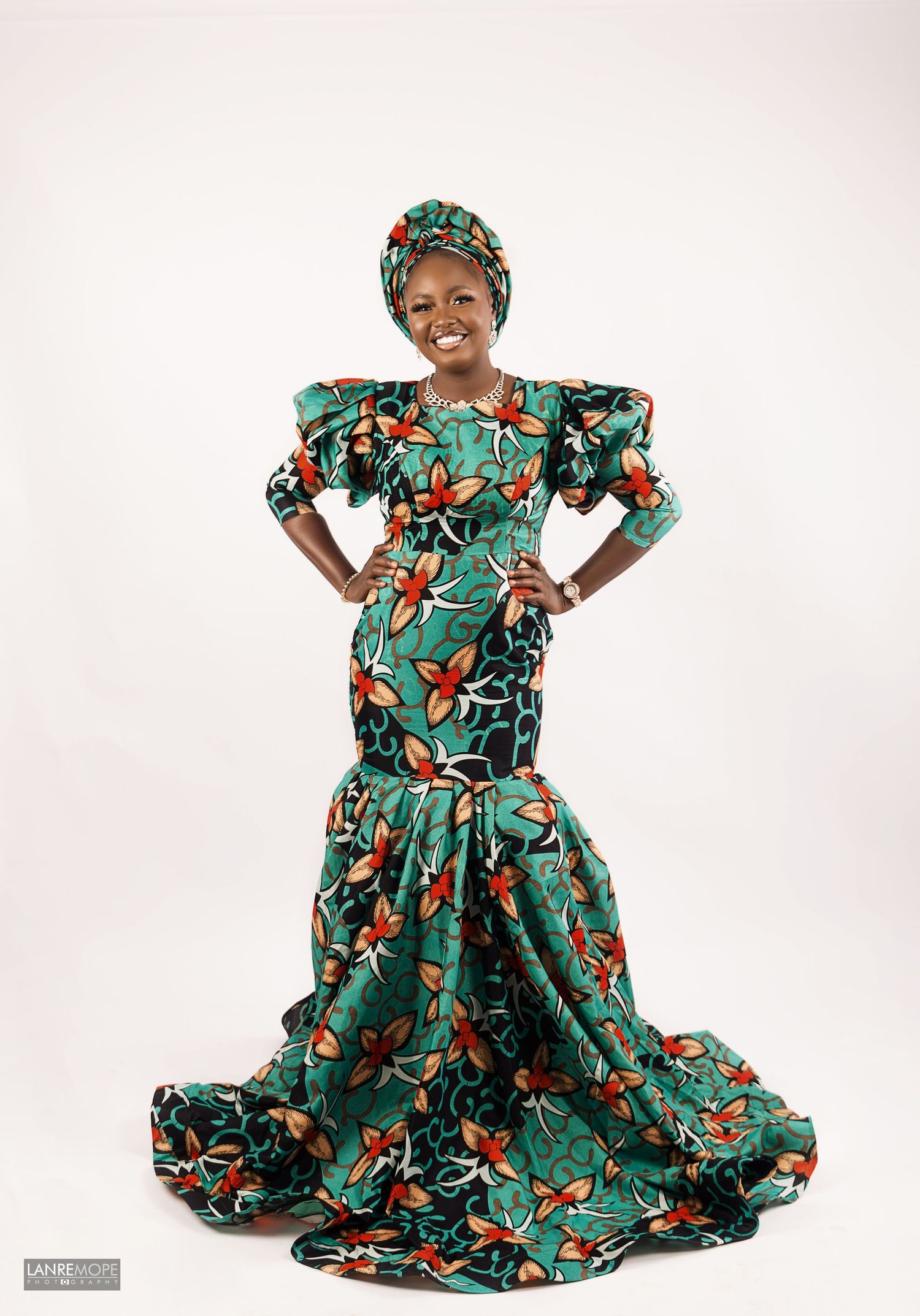 Woman smiling confidently in vibrant green floral African ankara mermaid dress with matching headwrap.