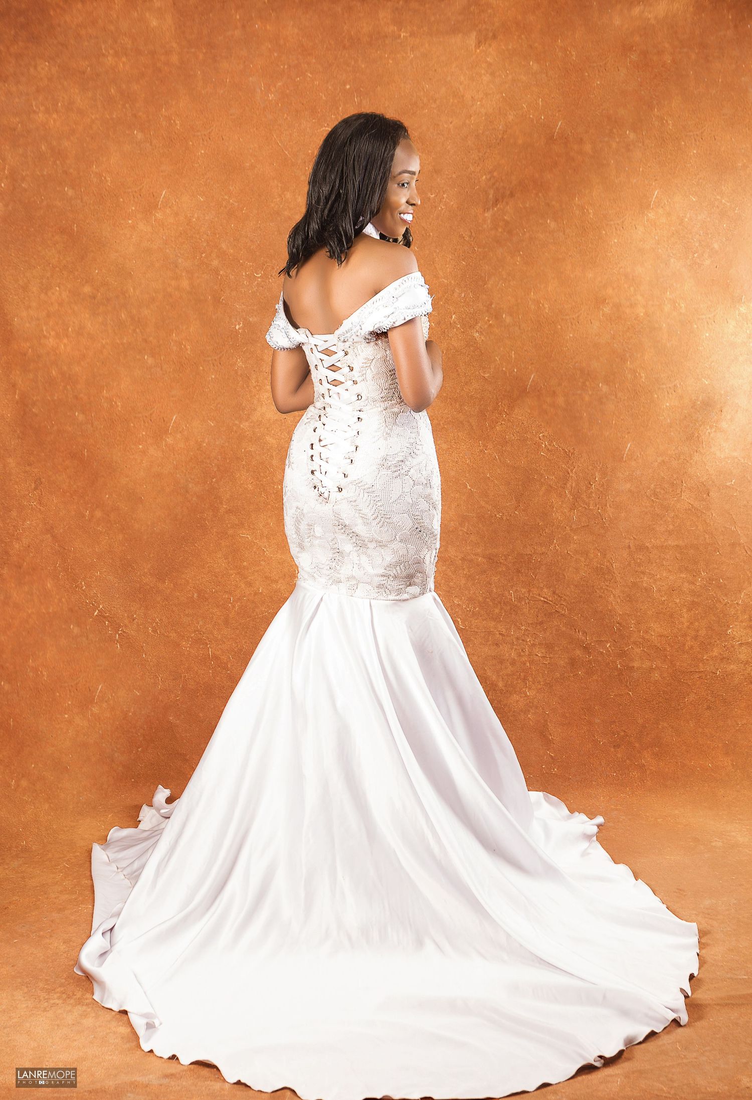 Bride in elegant white mermaid wedding gown with corset back and train in studio portrait.
