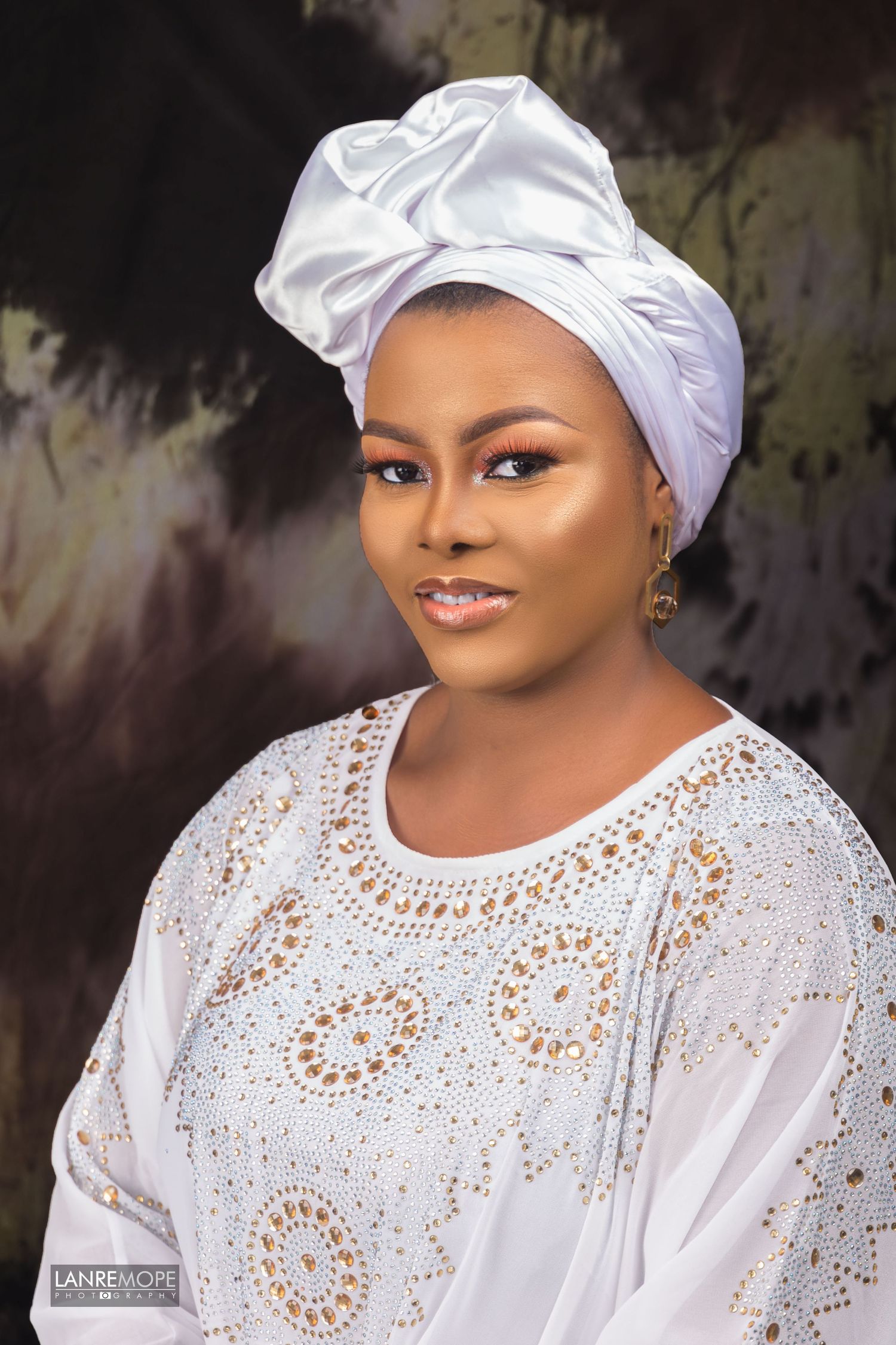 African woman in white embroidered blouse and white satin gele headwrap portrait.
