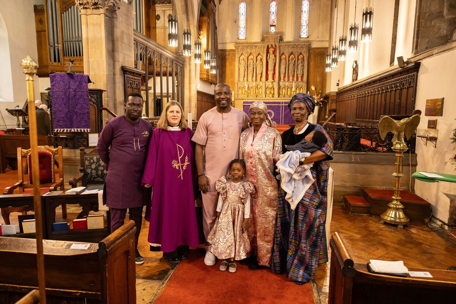 Family posing with a priest in colorful traditional Nigerian attire inside a historic church.