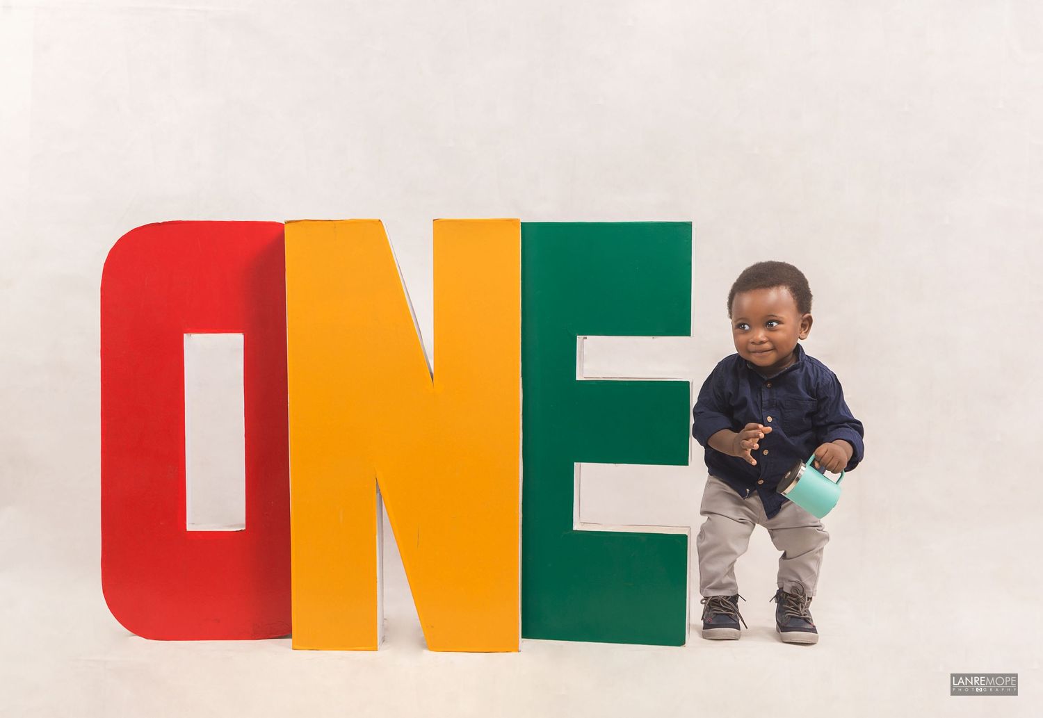 Toddler boy standing next to colorful ONE letters for first birthday photo shoot.