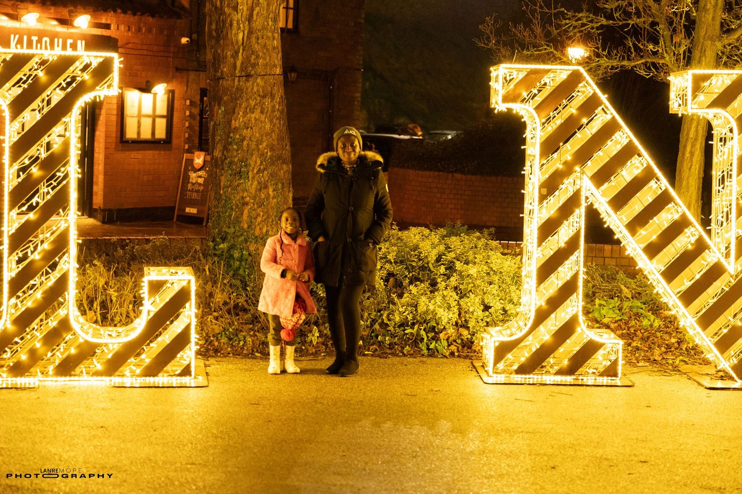 Two people standing in front of illuminated letter decorations at night during a festive holiday light display.