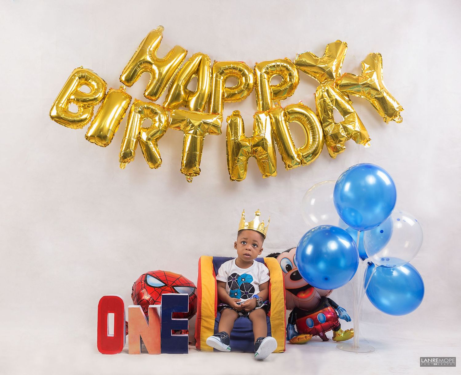 Toddler boy celebrating first birthday with Happy Birthday balloons and ONE letter blocks.