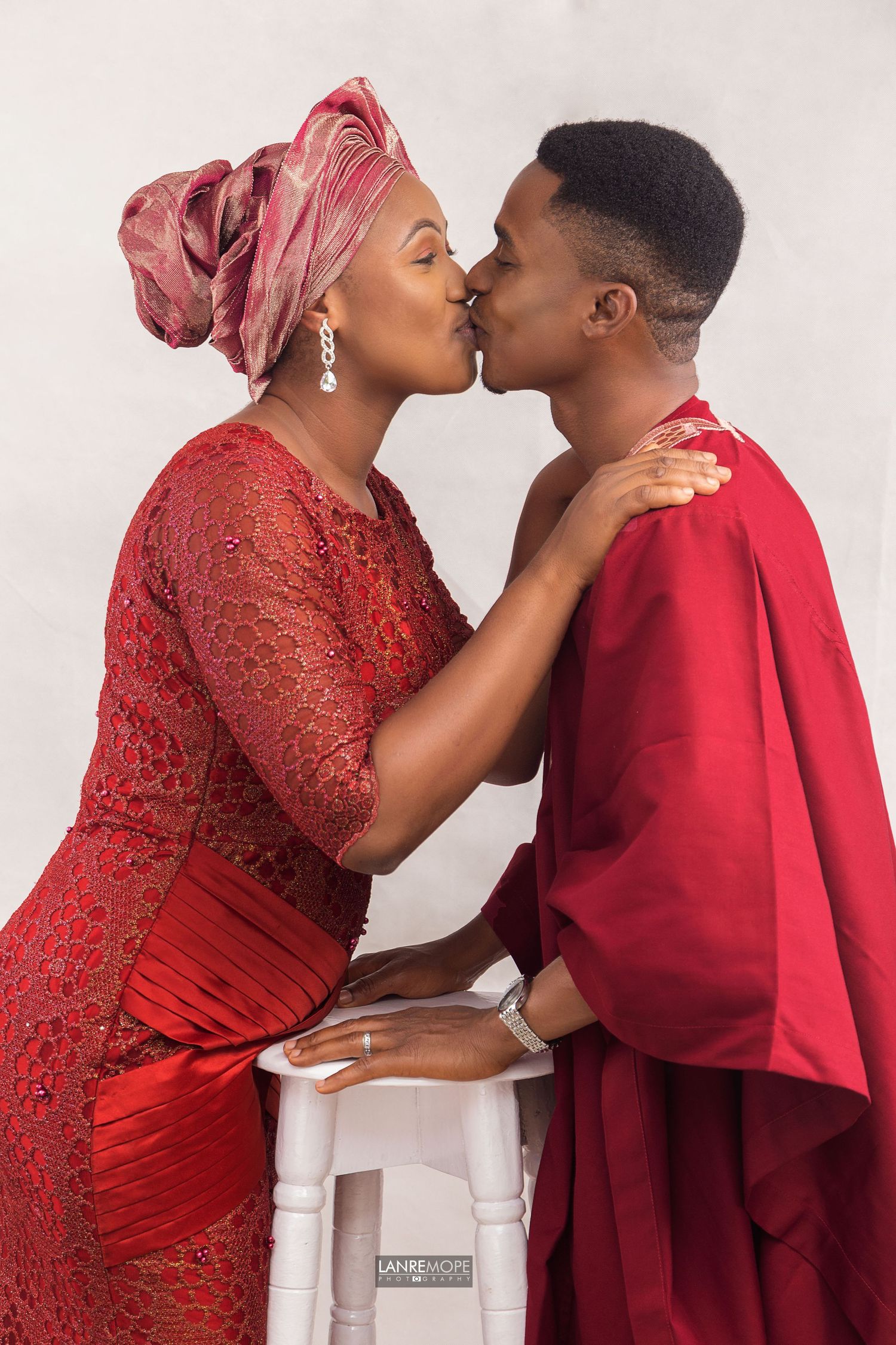 Nigerian couple in matching red traditional attire sharing a kiss during pre-wedding photo session.