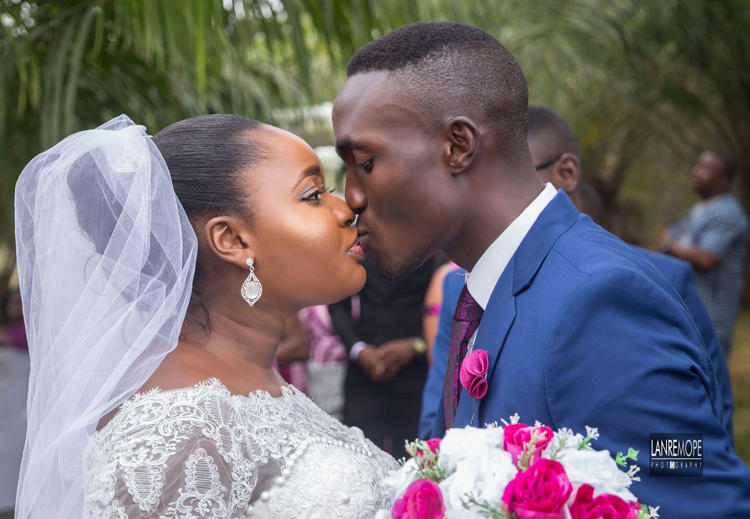 Newlywed couple sharing a romantic kiss at their wedding, bride holding a bouquet of pink flowers.
