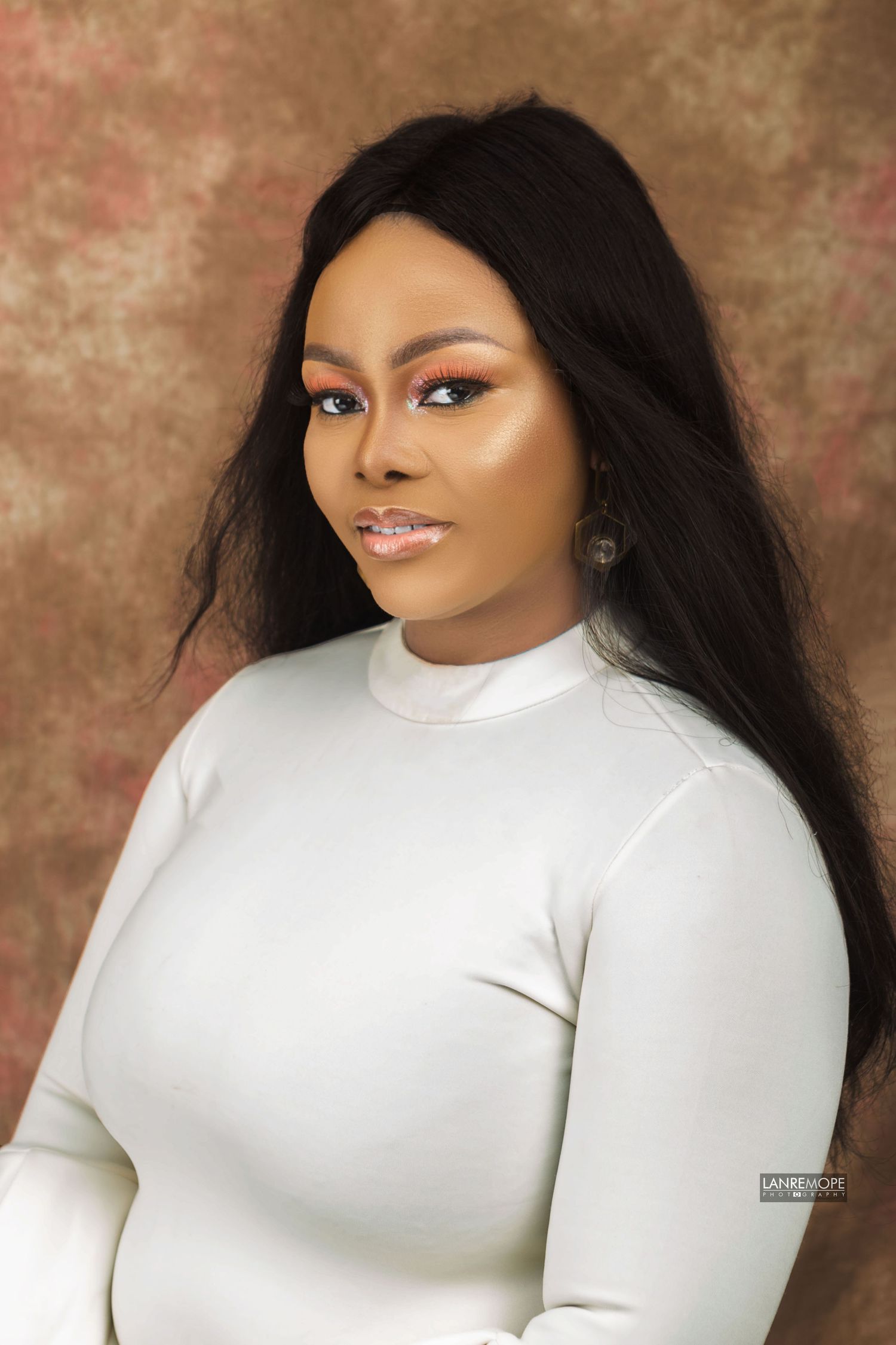 Woman with long black hair wearing white turtleneck posing for professional studio portrait photograph.