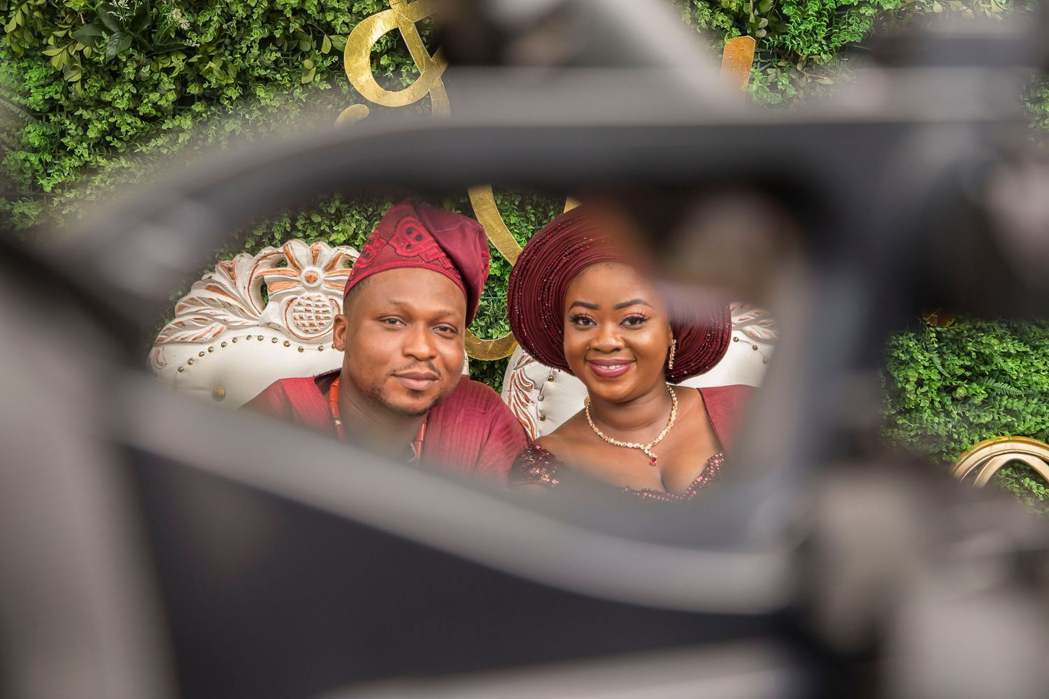 African couple in matching burgundy traditional attire photographed through a creative frame perspective.