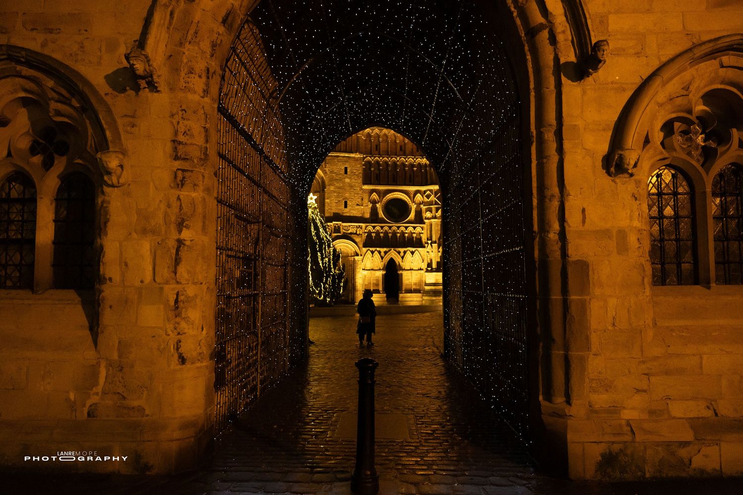 Night view through a stone archway illuminated in golden light revealing a historic cathedral beyond.