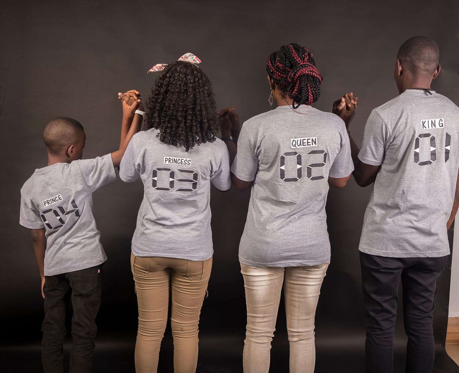 Family of four posing in matching gray t-shirts with King, Queen, Princess, and Prince labels on the back.