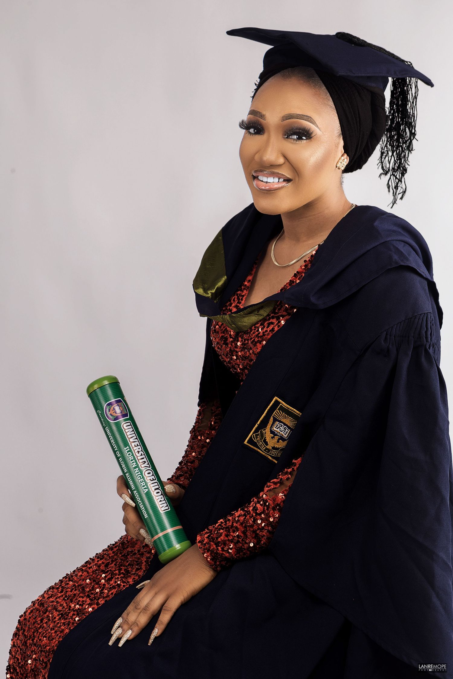Smiling woman in graduation cap and gown holding diploma tube for university graduation portrait.
