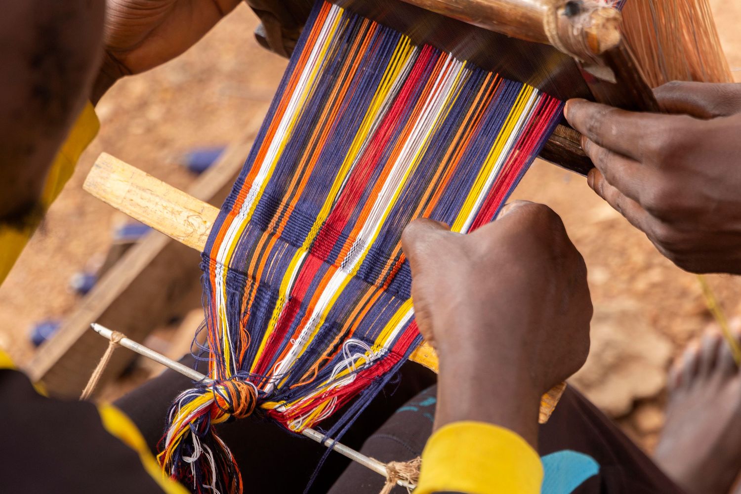 Close-up of hands weaving colorful striped fabric on a traditional loom outdoors.
