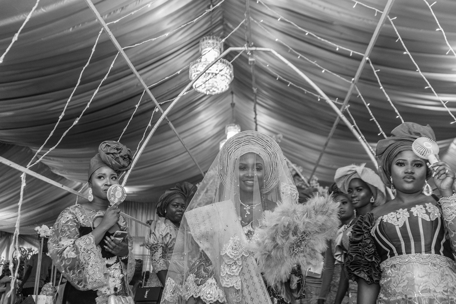 Black and white photo of a veiled Nigerian bride walking with attendants at her traditional wedding.