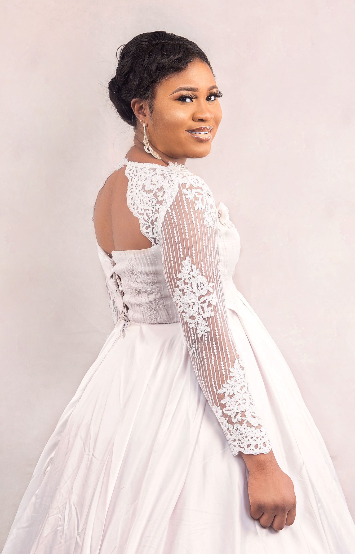 Elegant bride posing in a white lace long-sleeve ball gown wedding dress with corset back detail.