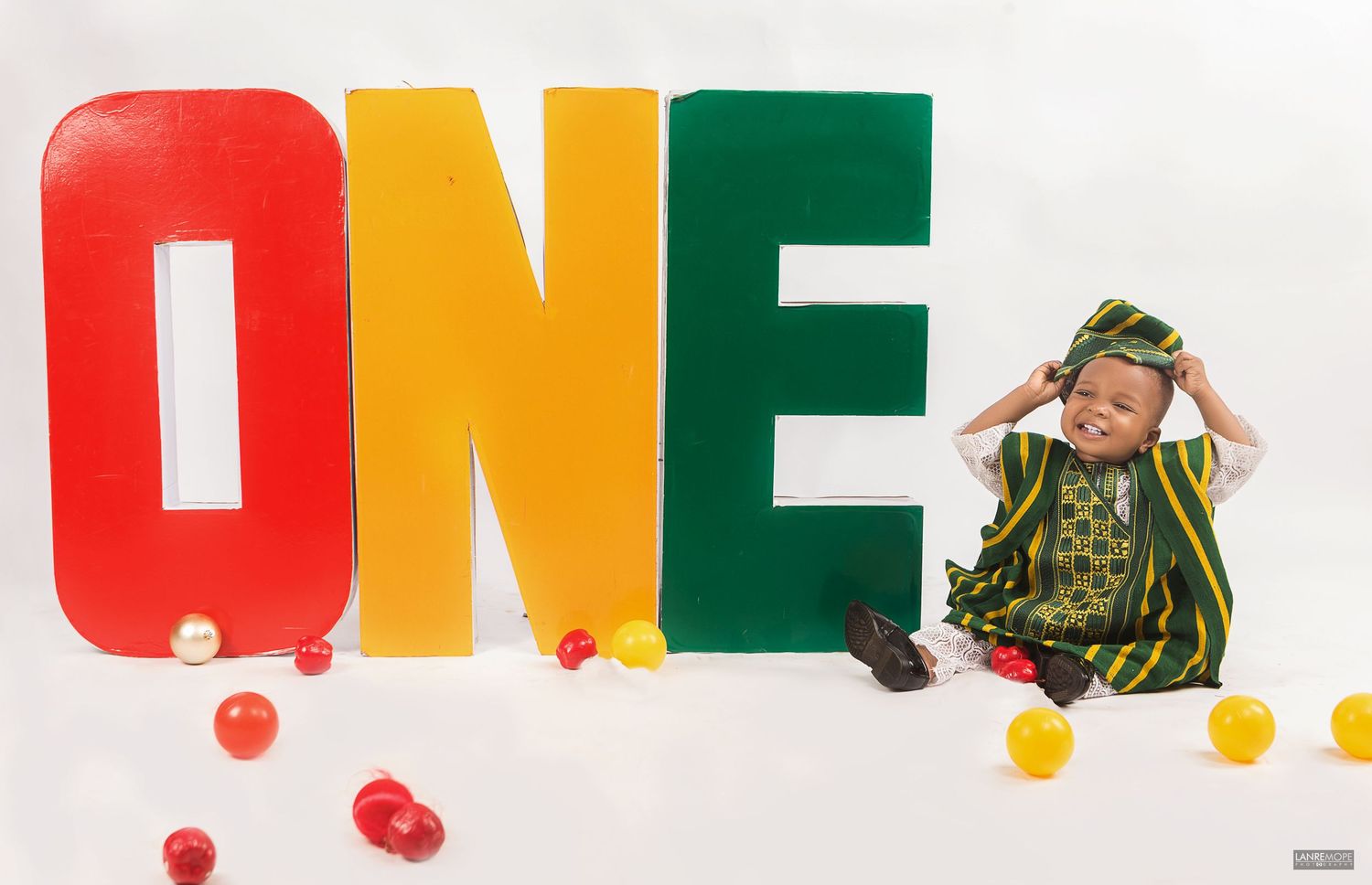 Cute baby in traditional Nigerian outfit celebrating first birthday beside colorful ONE letter props.