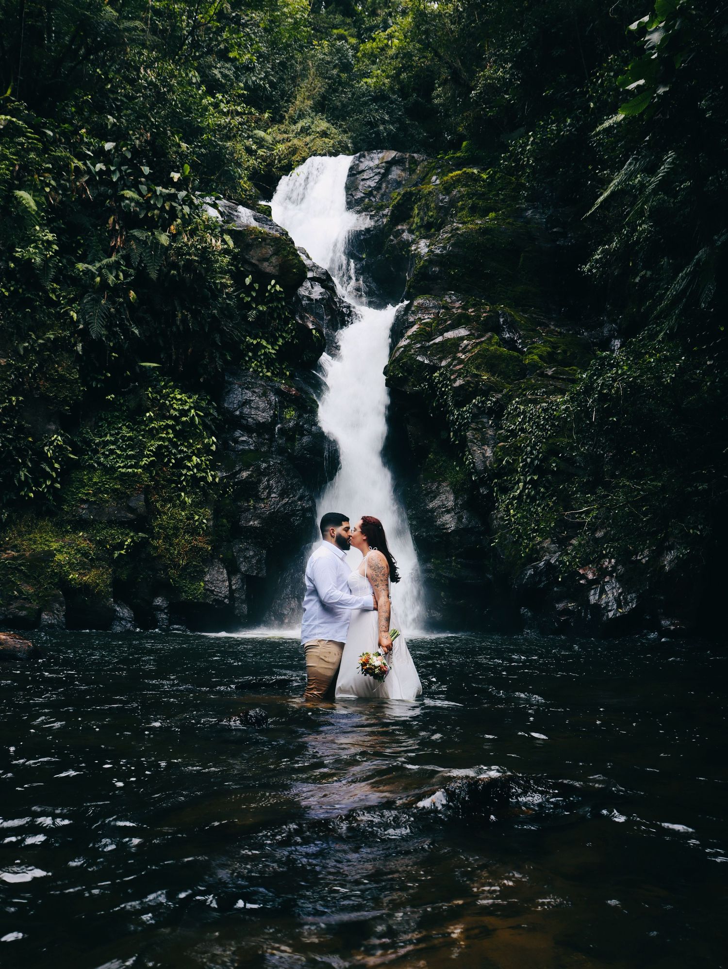 Casal de noivos em meio a cachoeira do chá na cidade de Tapirai durante ensaio pós casamento.