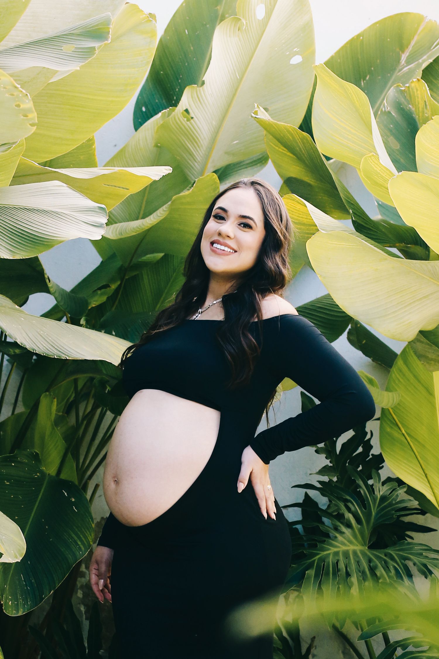 Gestante em ensaio fotográfico cercada por vegetação.