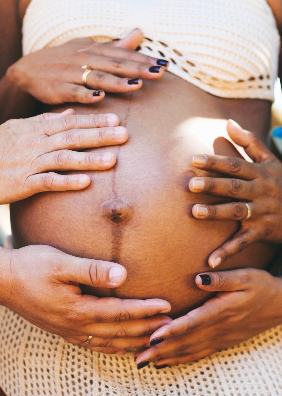 Mãos envolvendo a barriga de uma gestante em um momento de carinho no ensaio de fotos.