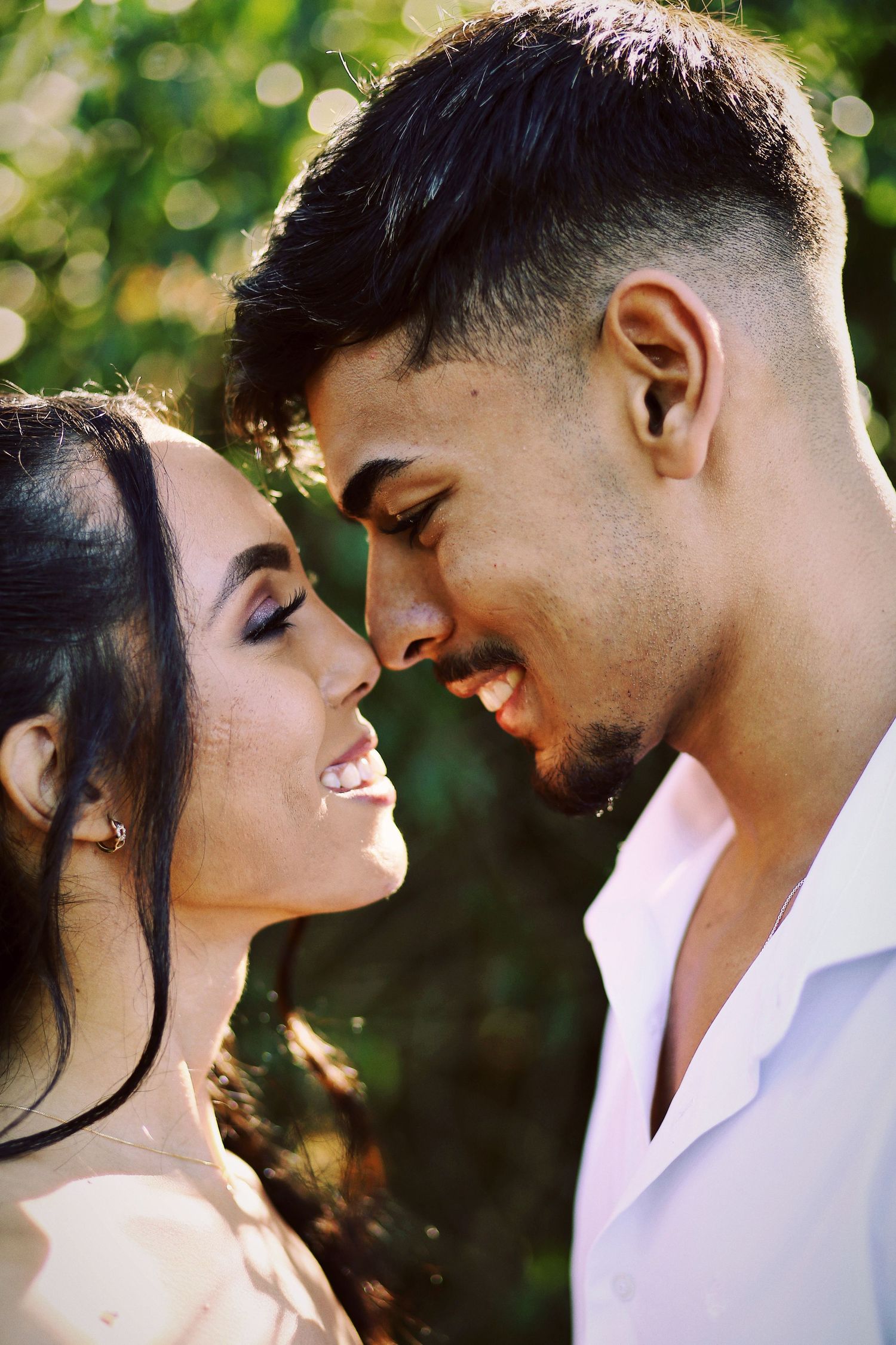Casal sorrindo com as testas e os narizes encostados.