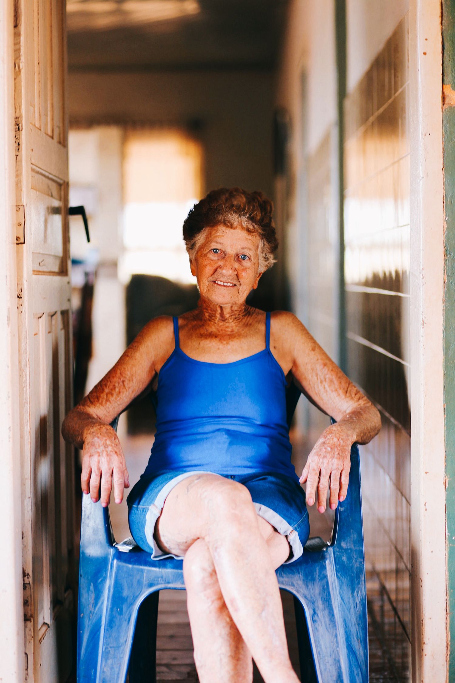 Senhora sentada em uma cadeira em frente à sua casa, em registro documental.