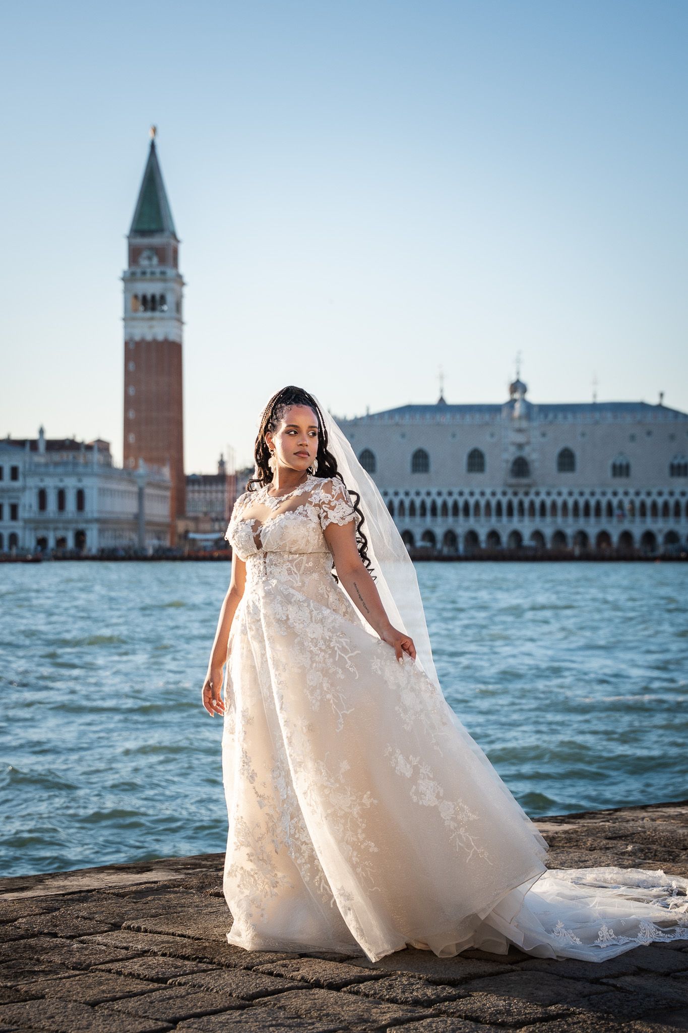 Bride in lace gown posing before Venice's iconic St. Mark's Square waterfront.