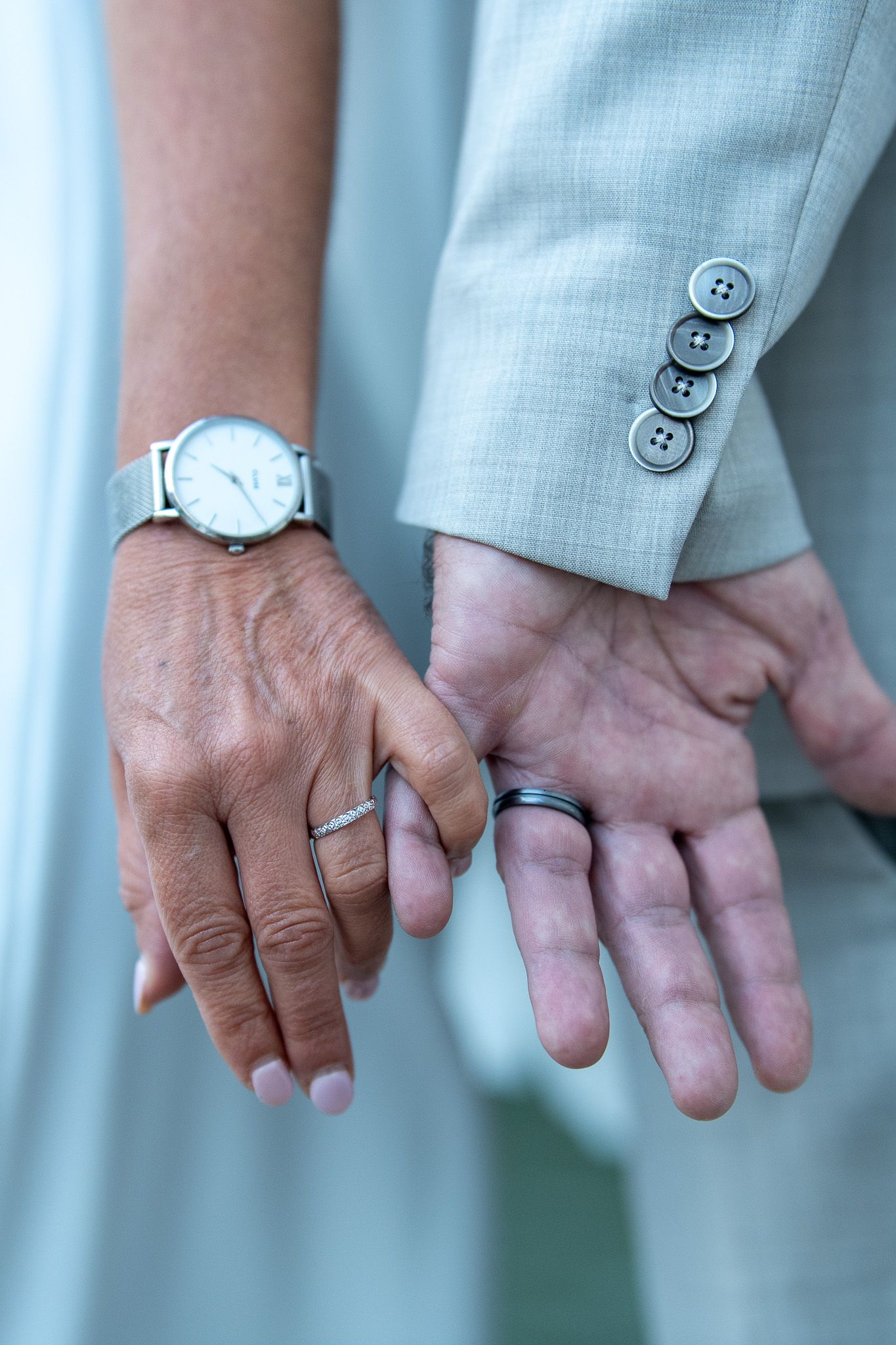 Close-up of newlyweds hands displaying wedding rings and elegant wristwatch.