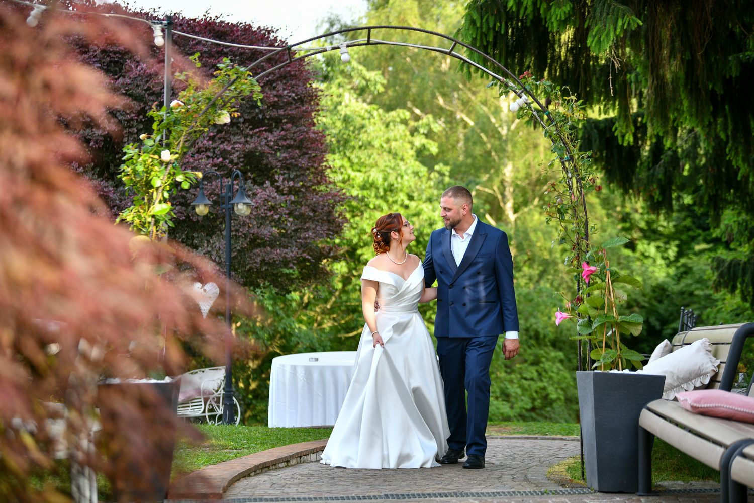 Bride and groom walking under a floral arch in a lush garden wedding venue.
