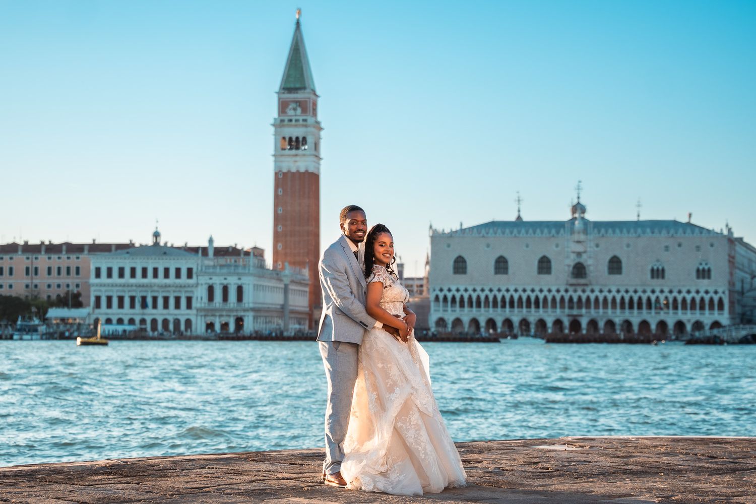Couple in wedding attire posing by the Grand Canal with St. Mark's Campanile and Doge's Palace in Venice.
