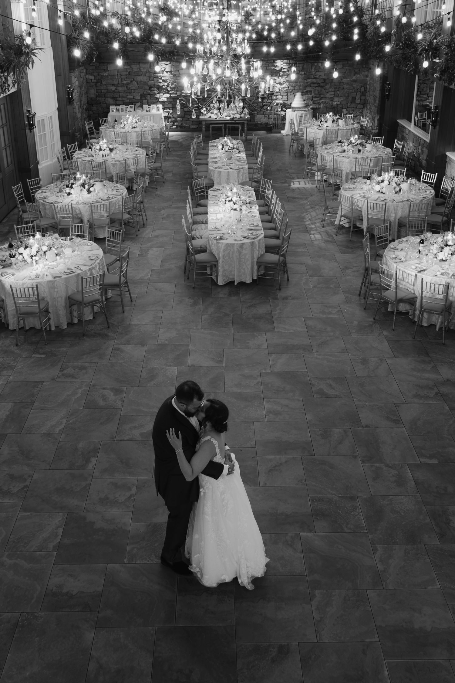 Bride and groom share first dance in elegant black and white wedding reception hall with lights.