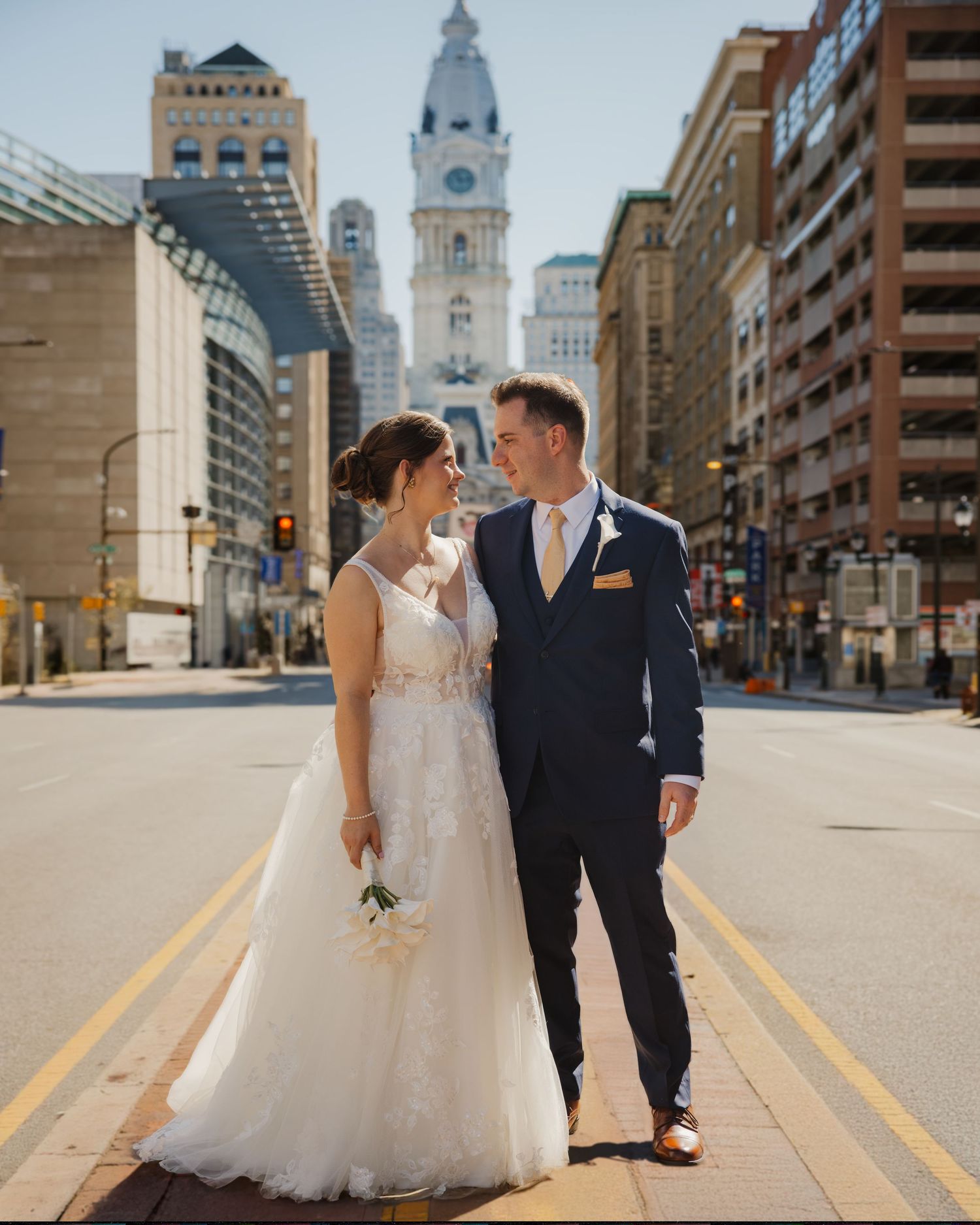 Bride and groom pose on a city street with Philadelphia City Hall in the background on their wedding day.