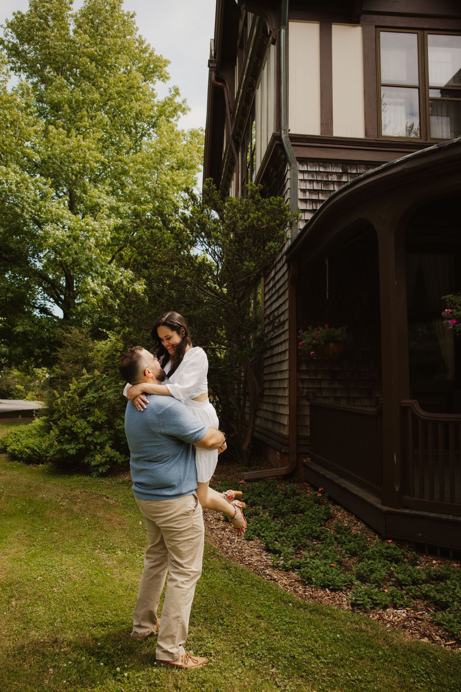 A man lifts his smiling partner in his arms outside a charming Tudor-style home.