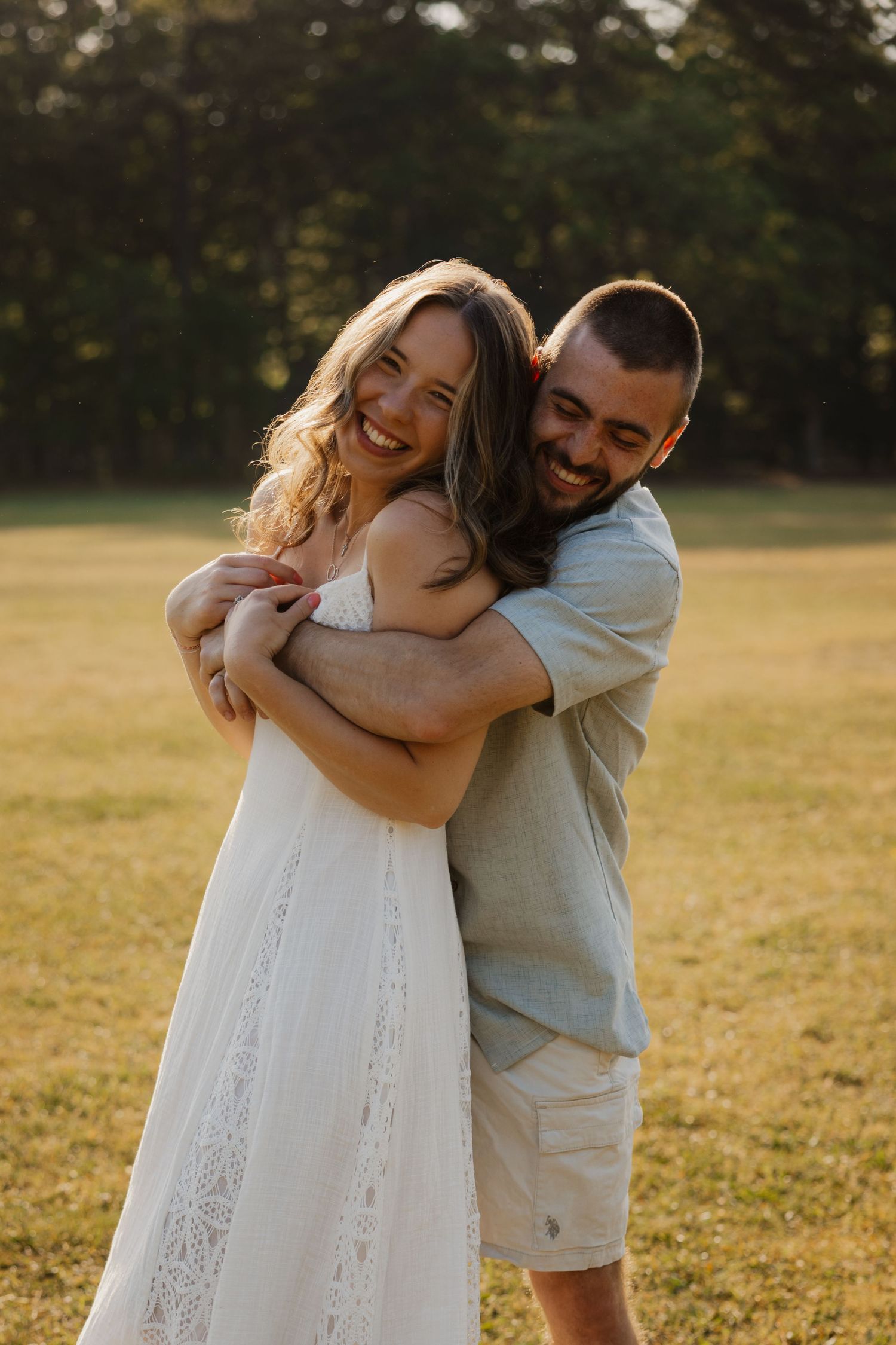 A laughing couple embraces in a sun-drenched open field with golden trees in the background.