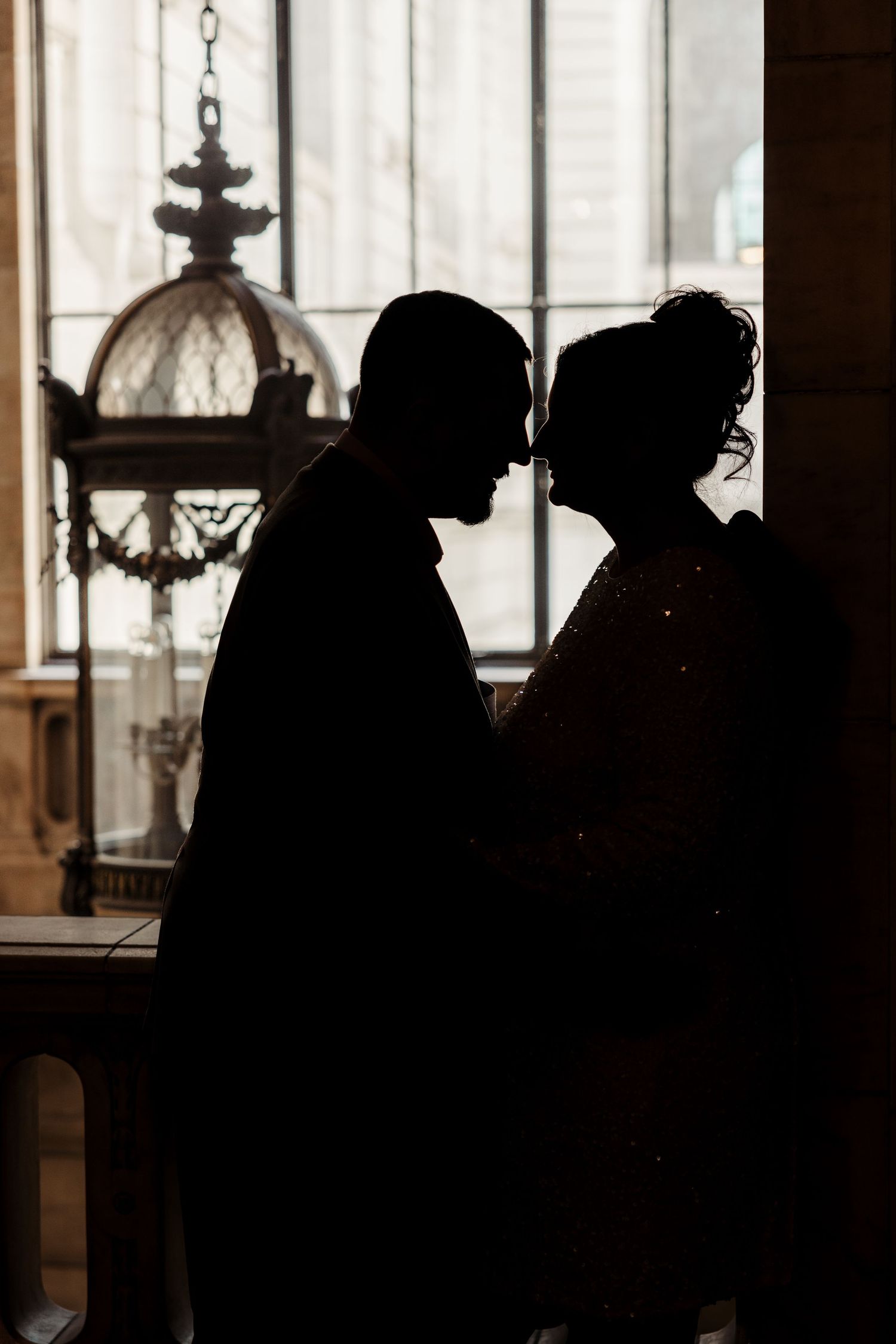 Romantic silhouette of couple facing each other near ornate window in dimly lit interior.