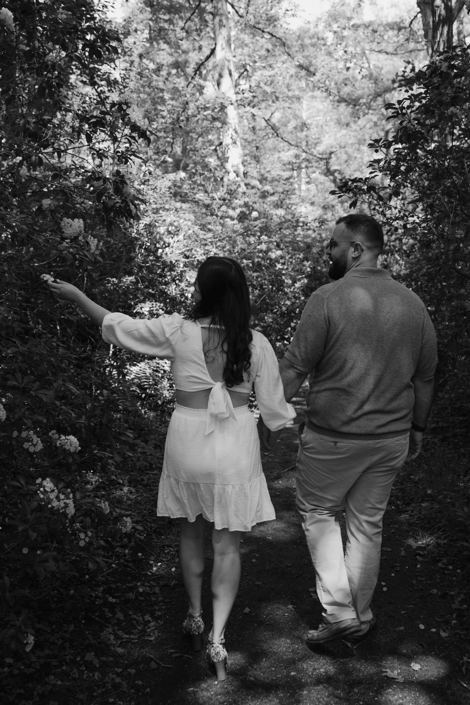 Black and white photo of a couple holding hands walking down a tree-lined garden path.