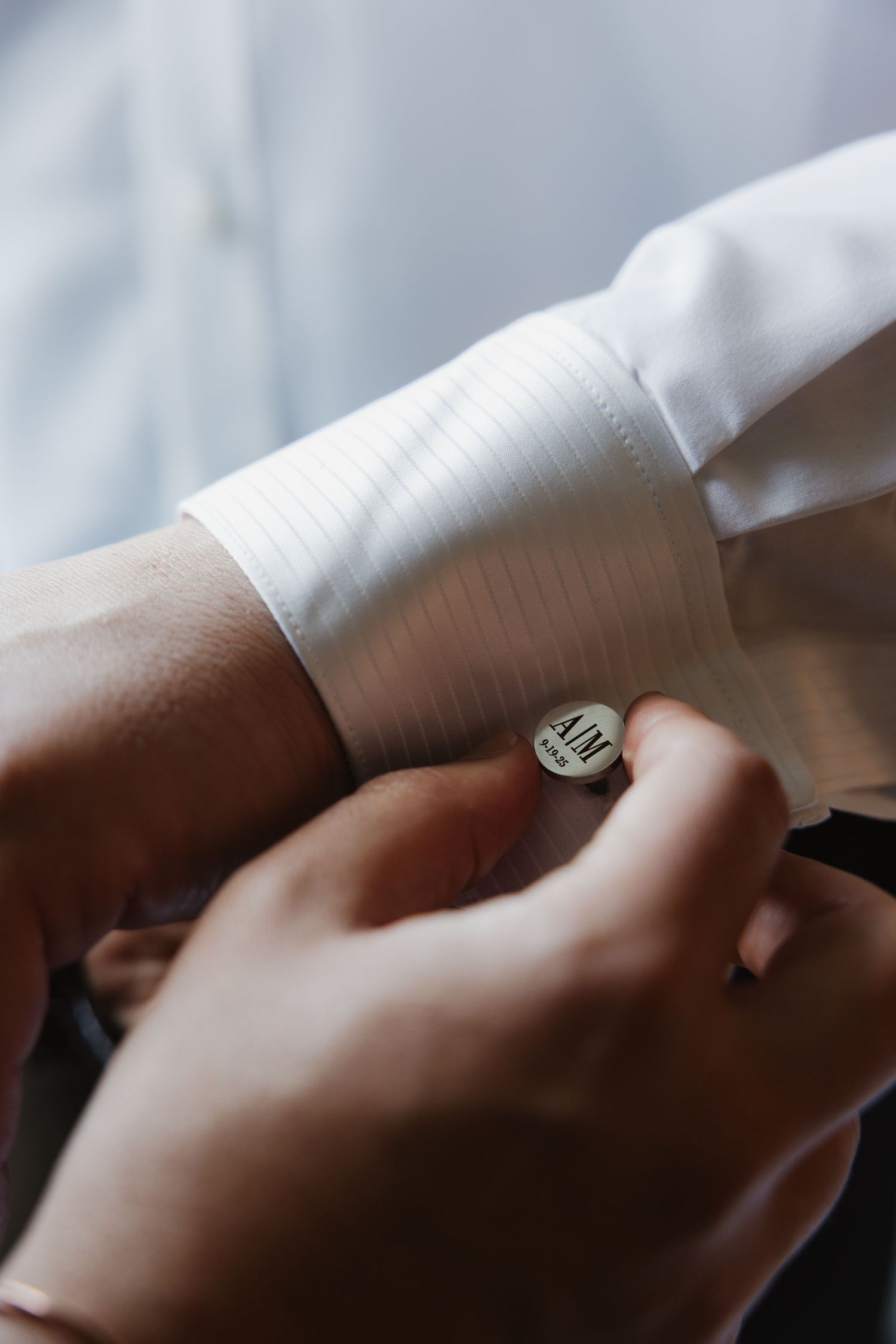 Close-up of personalized monogram cufflinks being fastened on groom's white dress shirt.