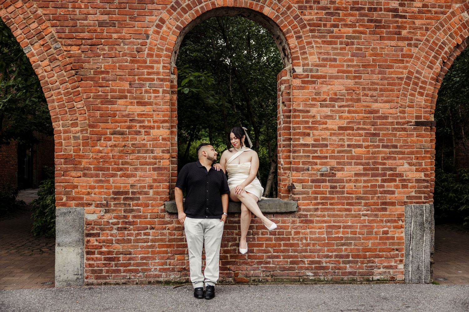Couple poses playfully against a rustic red brick archway during an engagement photo session.