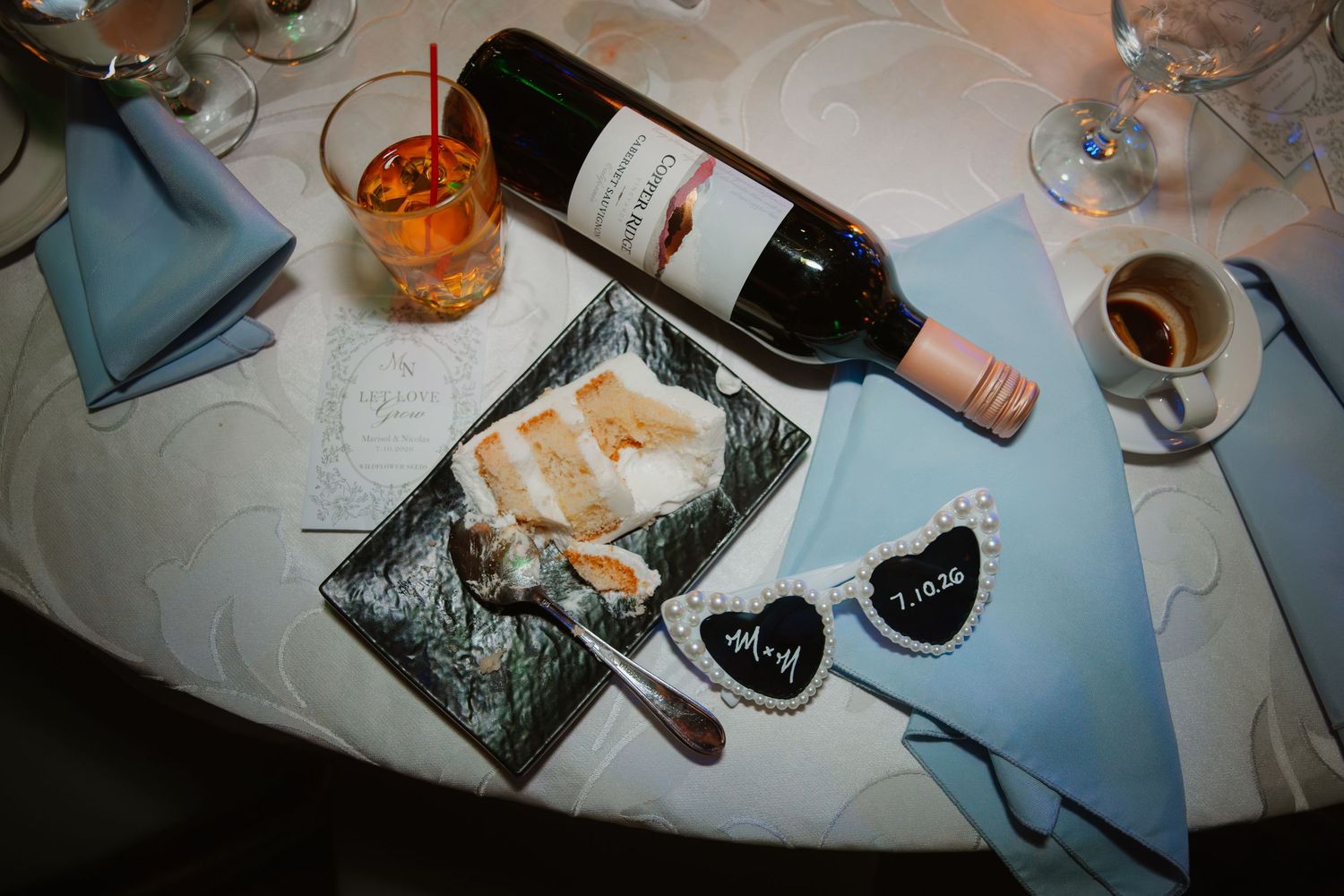 Wedding reception table detail with wine bottle, dessert plate, and personalized date decor.