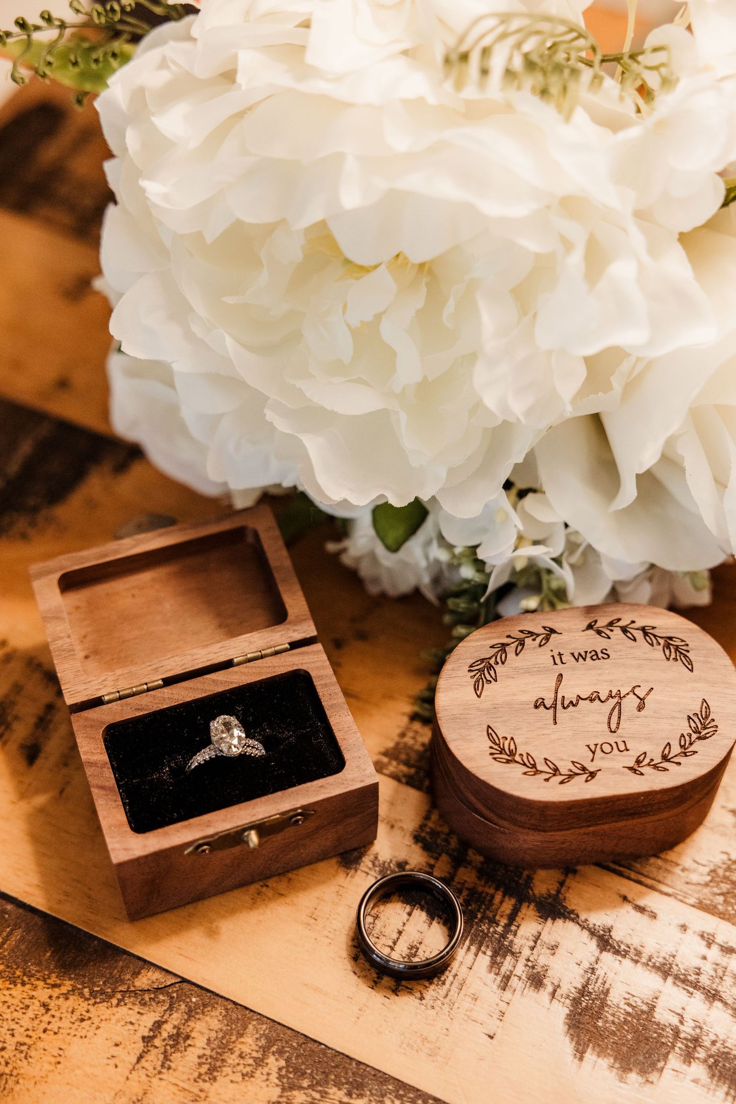 Diamond engagement ring in wooden box beside engraved it was always you ring box with white peonies.