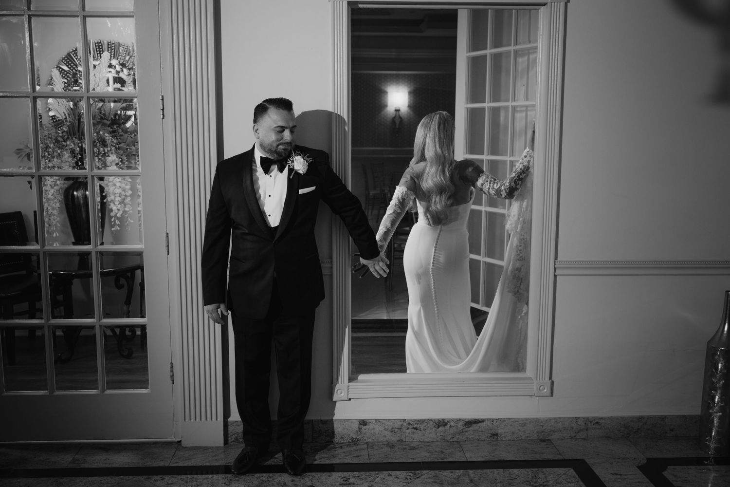 Black and white photo of bride and groom holding hands in elegant doorway.