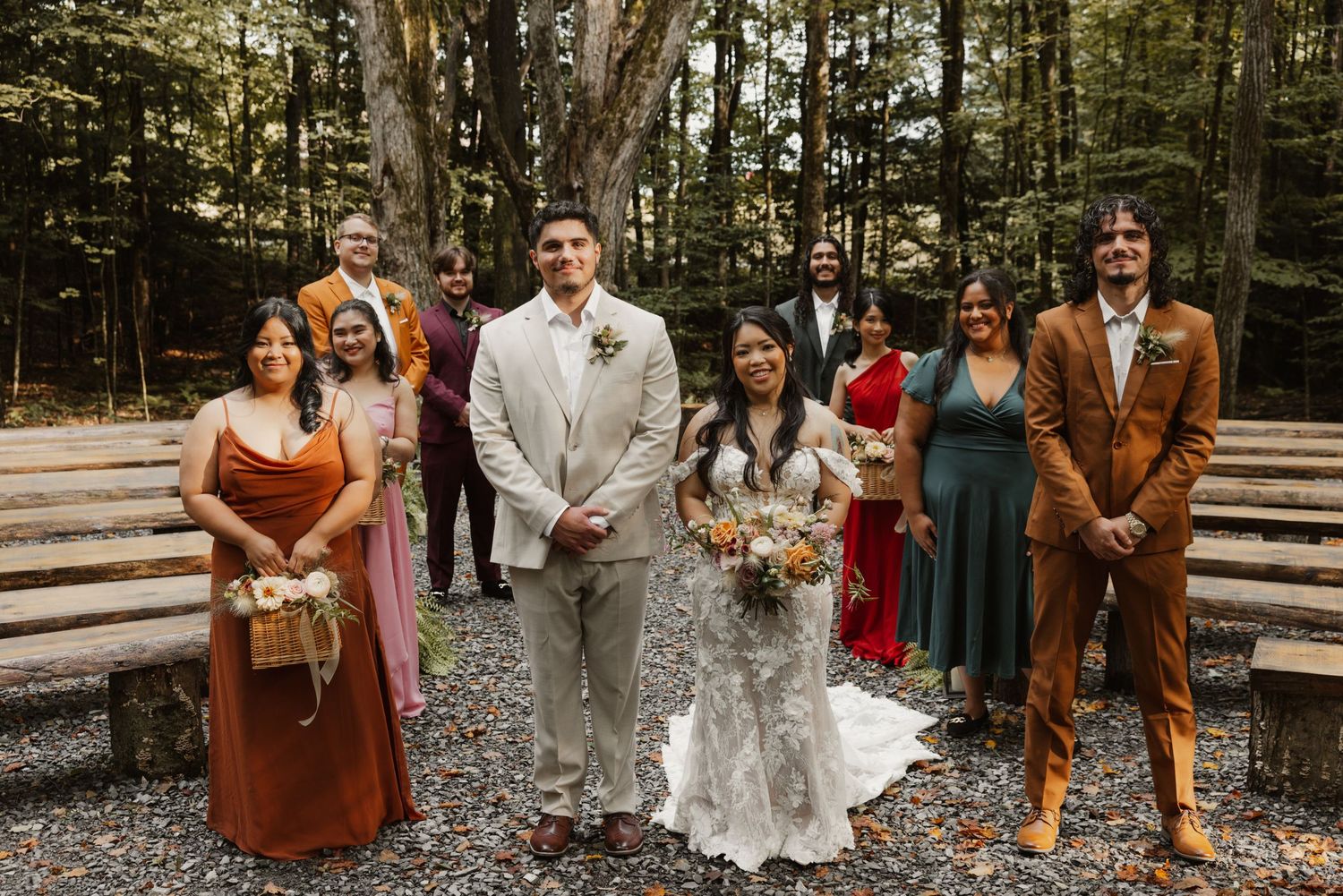 Wedding party poses together in colorful attire among autumn trees at a woodland outdoor ceremony venue.