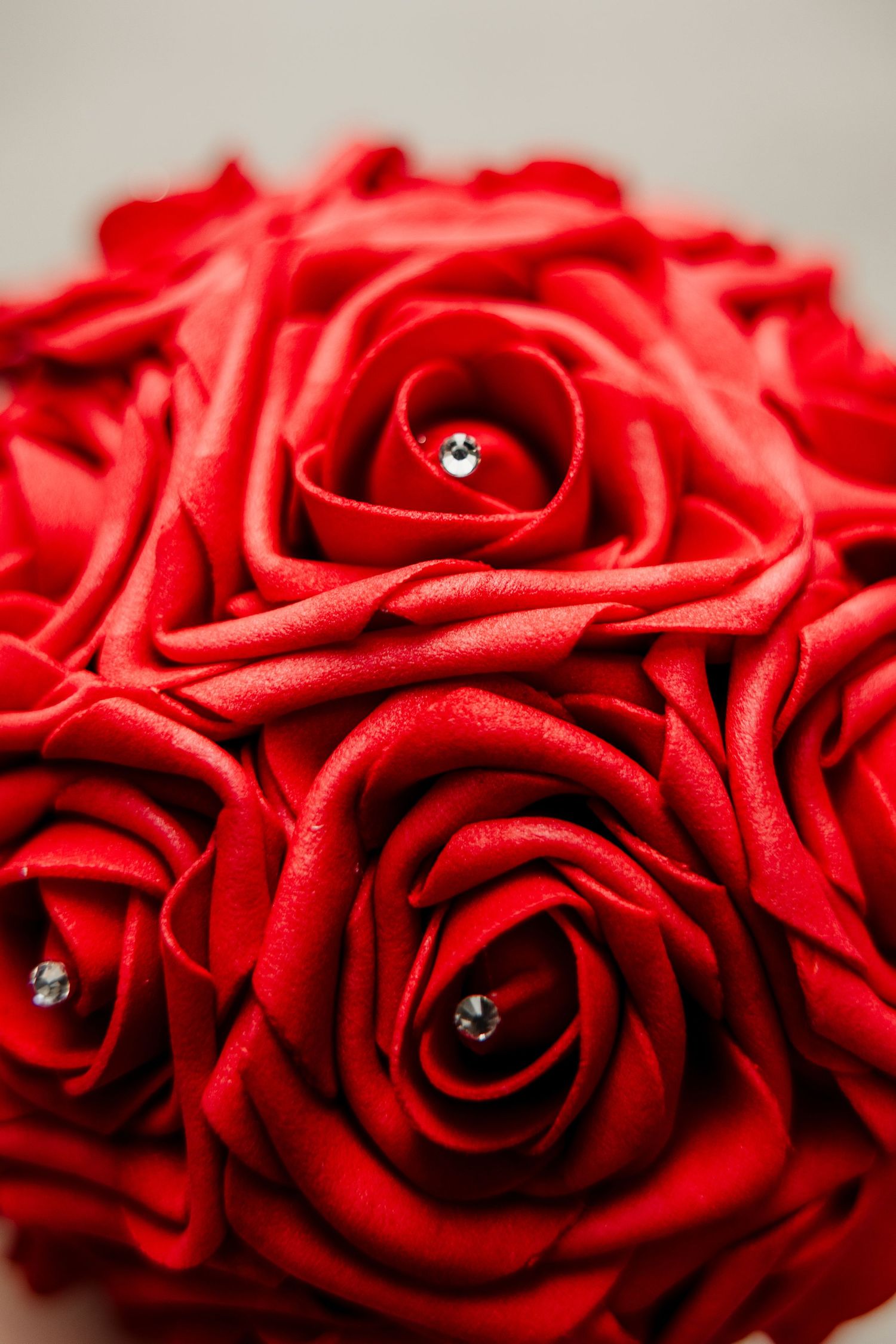 Close-up of a bridal bouquet made of red roses adorned with small diamond accents at the center.