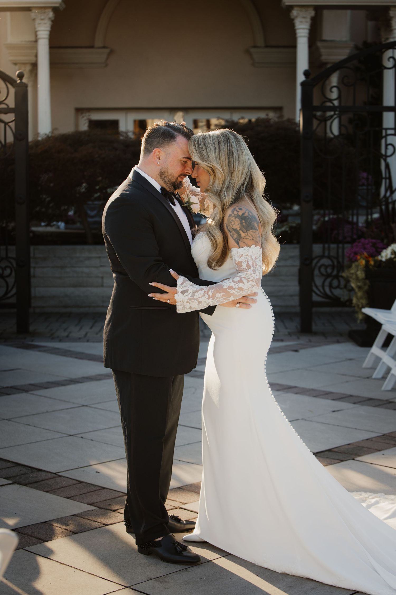Bride and groom embracing forehead to forehead in elegant wedding attire outside a grand venue.
