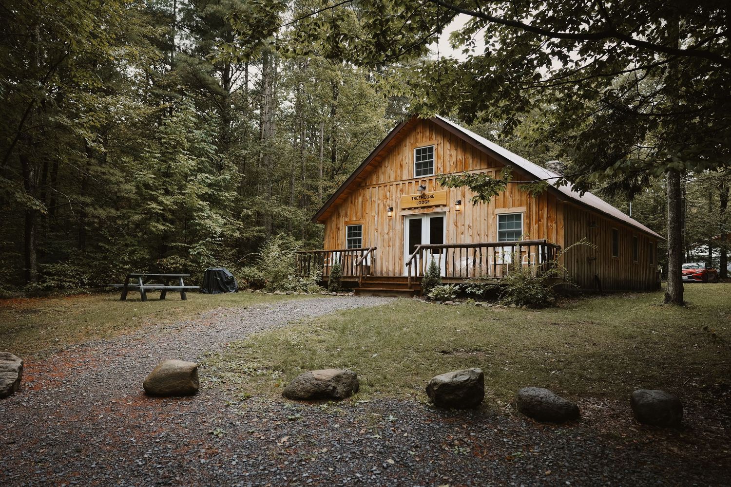 Rustic wooden barn cabin nestled in lush forest with stone pathway and picnic area.