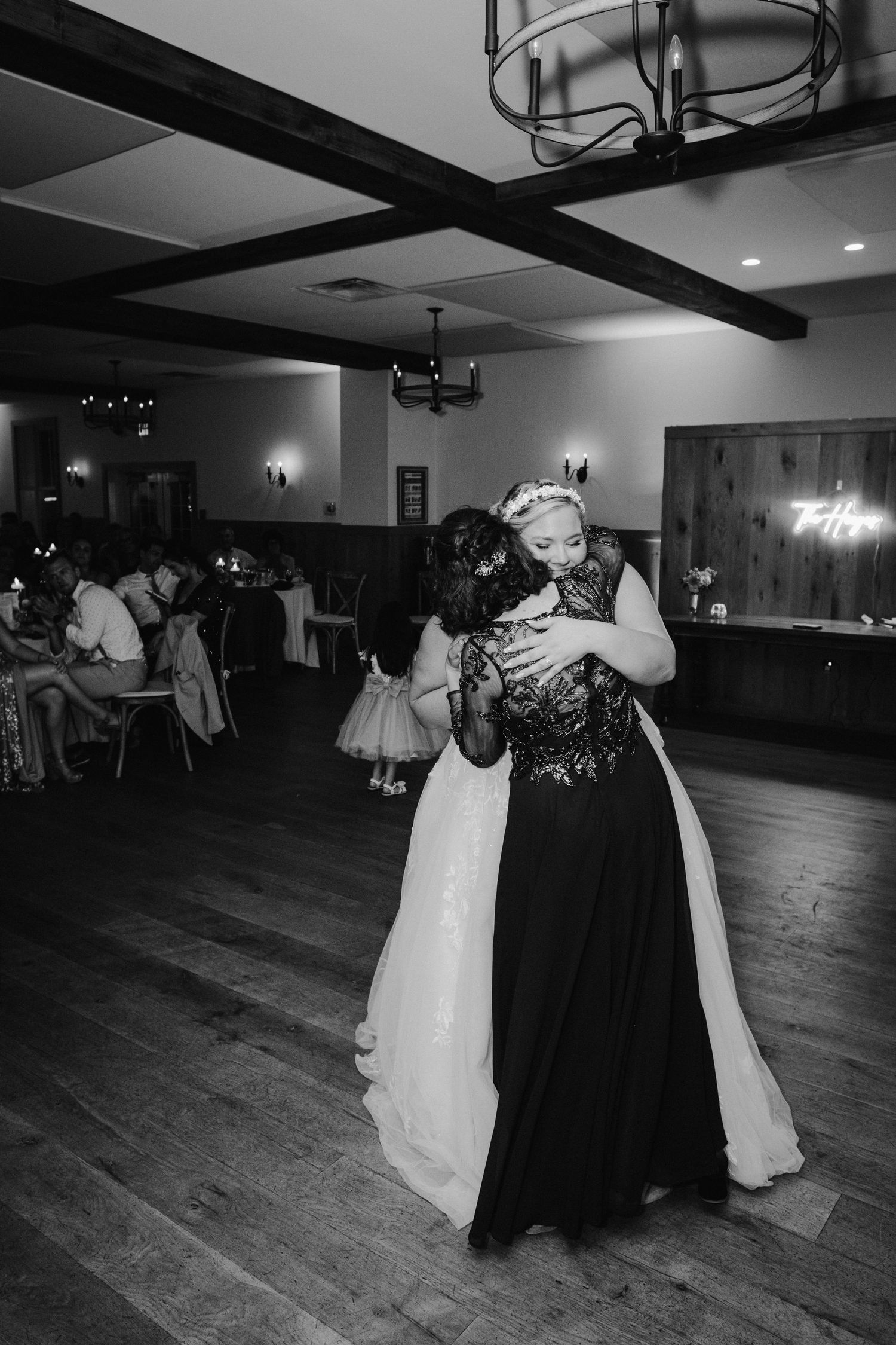 Black and white photo of bride and mother sharing emotional first dance embrace at wedding reception.