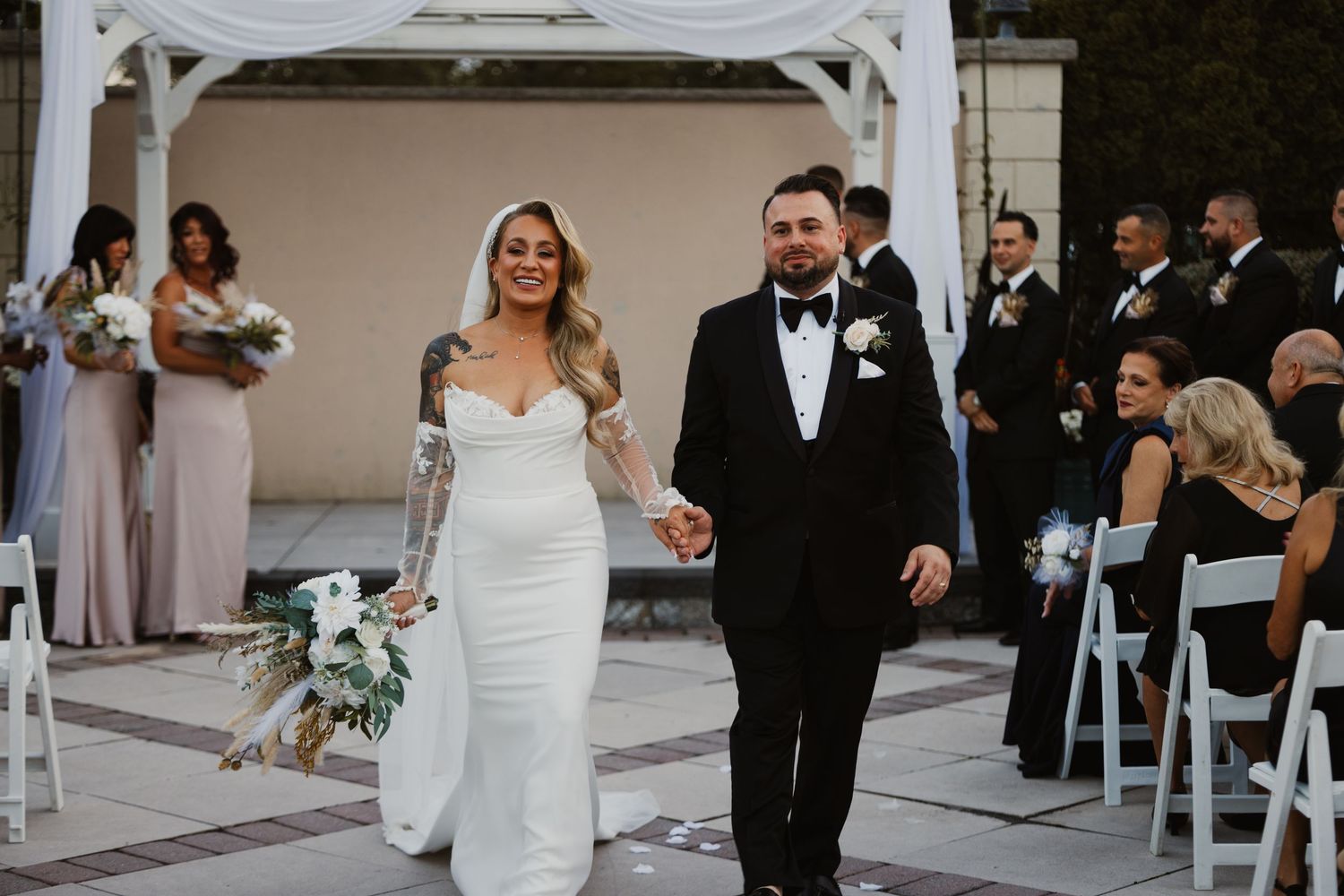 Newlyweds walk hand in hand down the aisle after their outdoor wedding ceremony surrounded by guests.